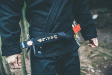 Cargar imagen en el visor de la galería, Cinturón Kanji  &quot;Un cinturón blanco que nunca se rindió&quot; - Negro con barra Roja - StockBJJ
